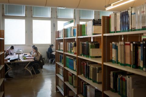 Des étagères de livres et trois étudiants en train de travailler assis autour d'une table